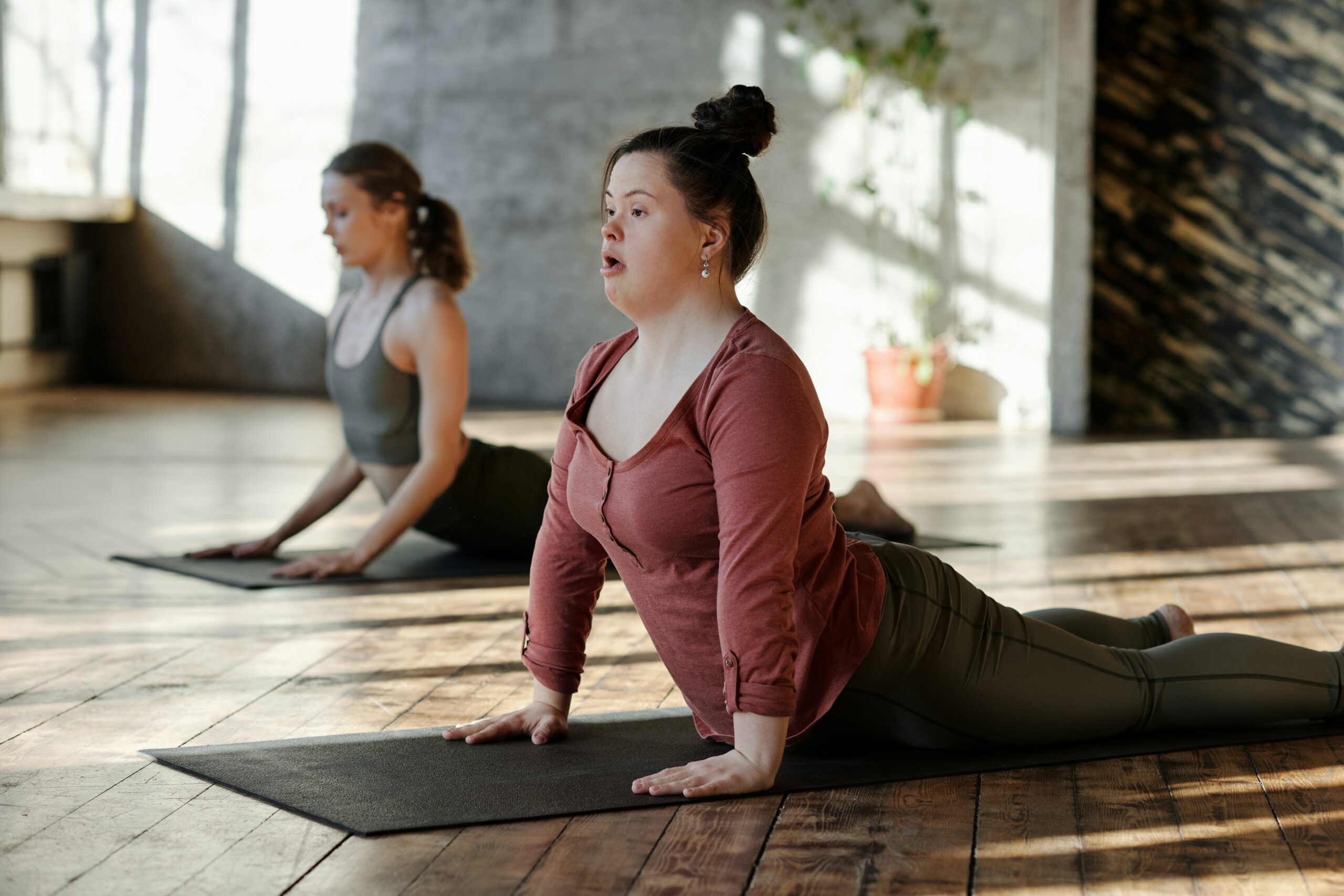 Zwei Menschen, darunter ein Down-Syndrom-Mädchen, machen Yoga in einem Kursraum